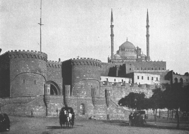 Black and white photograph of El Kala, Cairo, built by Saladin, 1166 A.D. A medieval fortress with crenellations and a mosque and two minarets in the background.